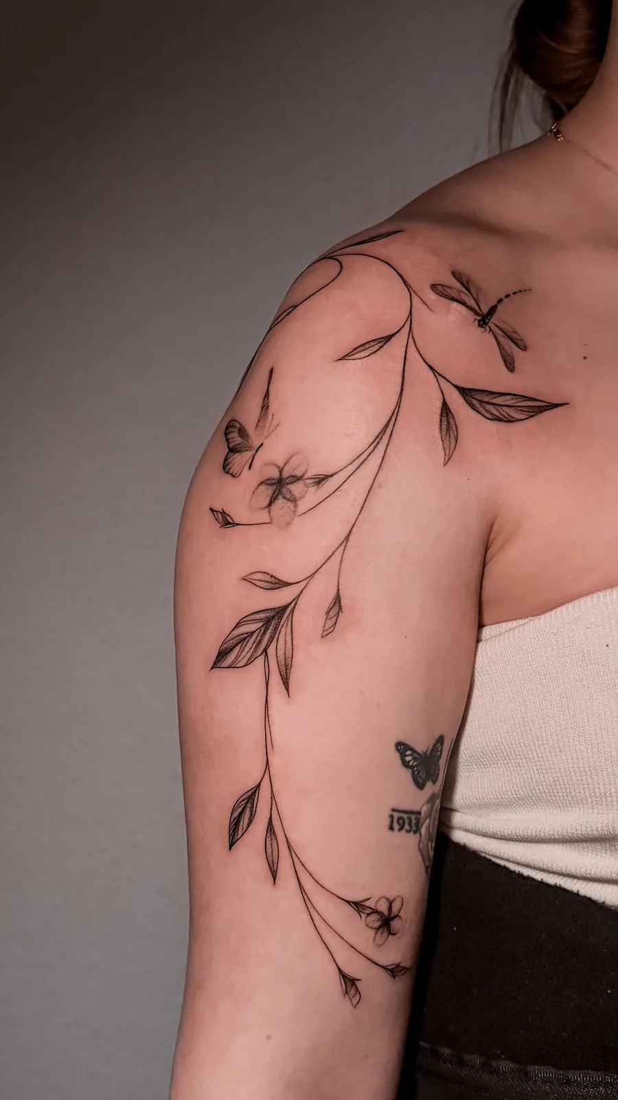 Blütenranke mit Libelle – Fineline Tattoo an Schulter und Oberarm, gestochen von Anna in Hamburg | Tattoo-Highlights